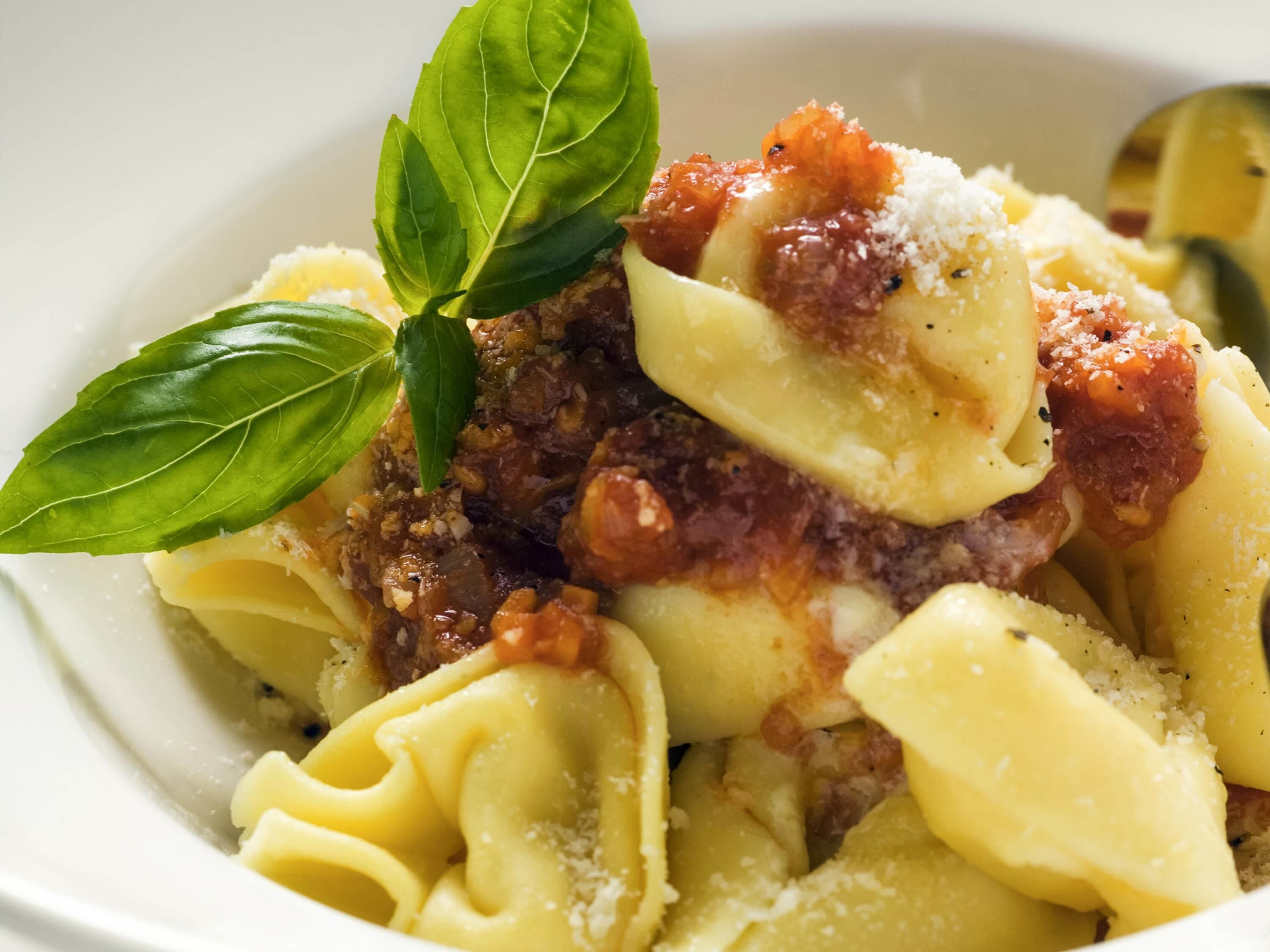 A bowl of pasta with a tomato-based sauce and grated cheese, garnished with basil leaves.