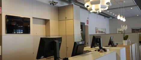 Un moderno mostrador de recepción con múltiples monitores de ordenador, una caja registradora y una máquina de café.