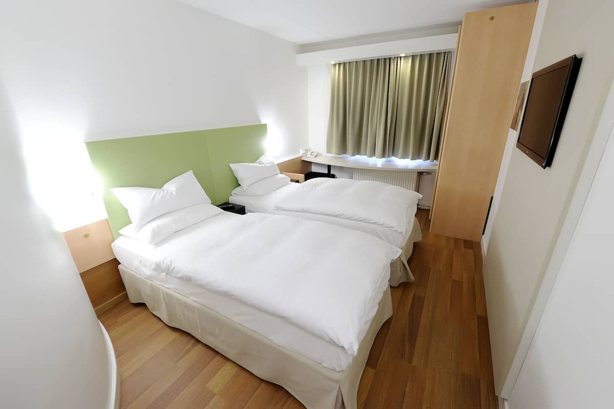 Hotellihuone, jossa on kaksi sänkyä, työpöytä ja ikkuna, jossa on verhot.
