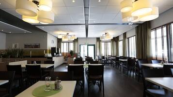 En rymlig restaurang med flera matbord och stolar, stora hängande lampor och utsikt över staden genom stora fönster.