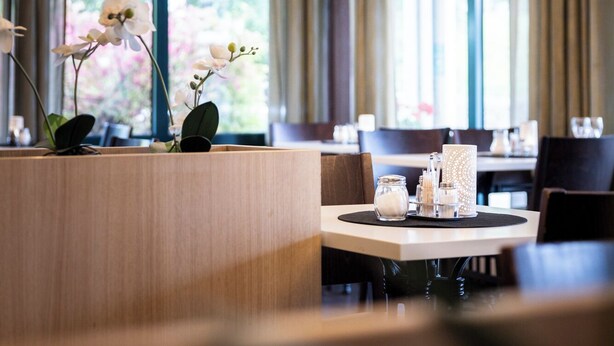 Un hall d’hôtel moderne avec une table ronde, un vase d’orchidées et un lustre.
