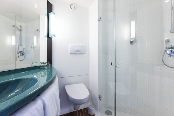 A modern bathroom with a glass shower enclosure, a white toilet, and a glass sink with a towel.