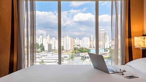 A hotel room with a large window offering a city view, a bed, a laptop, and a pair of glasses on the bed. - Lummina Ibirapuera São Paulo (Sao Paulo)