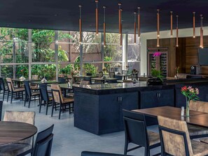 A modern restaurant with a central bar area, large windows offering views of greenery, and contemporary lighting fixtures. - Lummina Ibirapuera São Paulo (Sao Paulo)