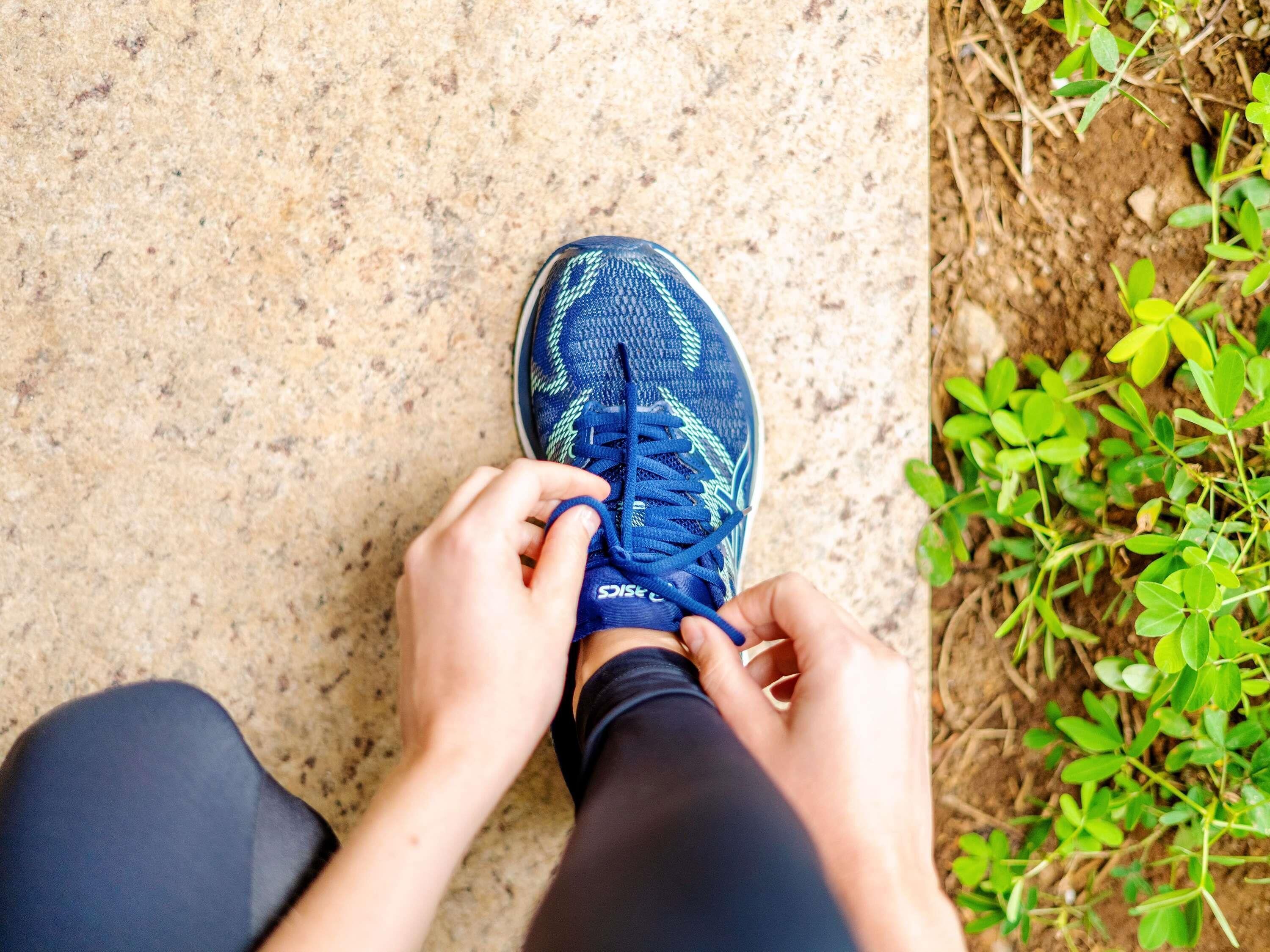 A person tying blue athletic shoes on a textured surface.