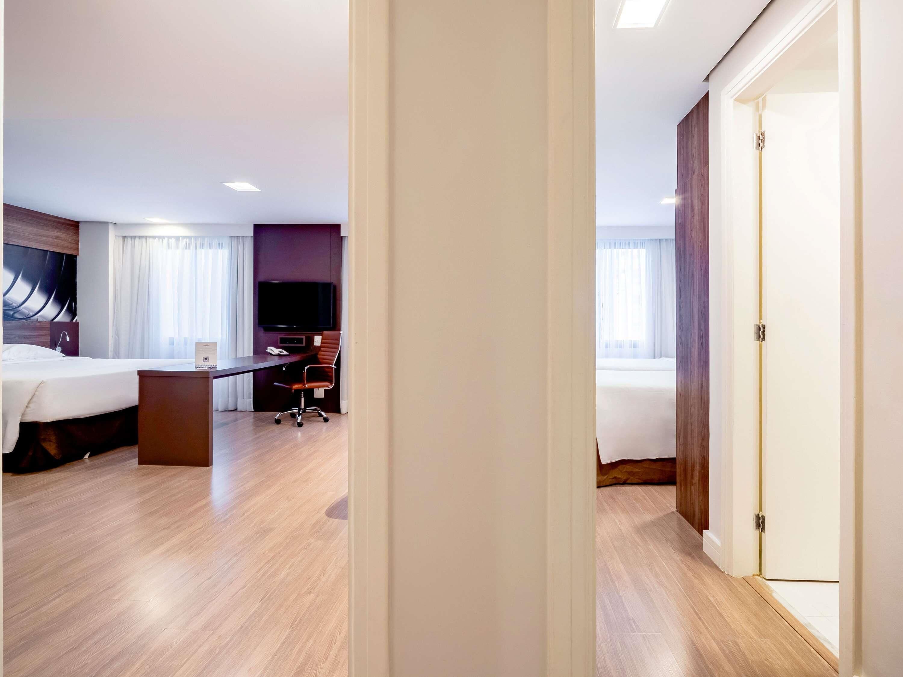 A hotel room with a bed, desk, chair, television, and a door.