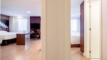 A hotel room with a bed, desk, chair, television, and a door.