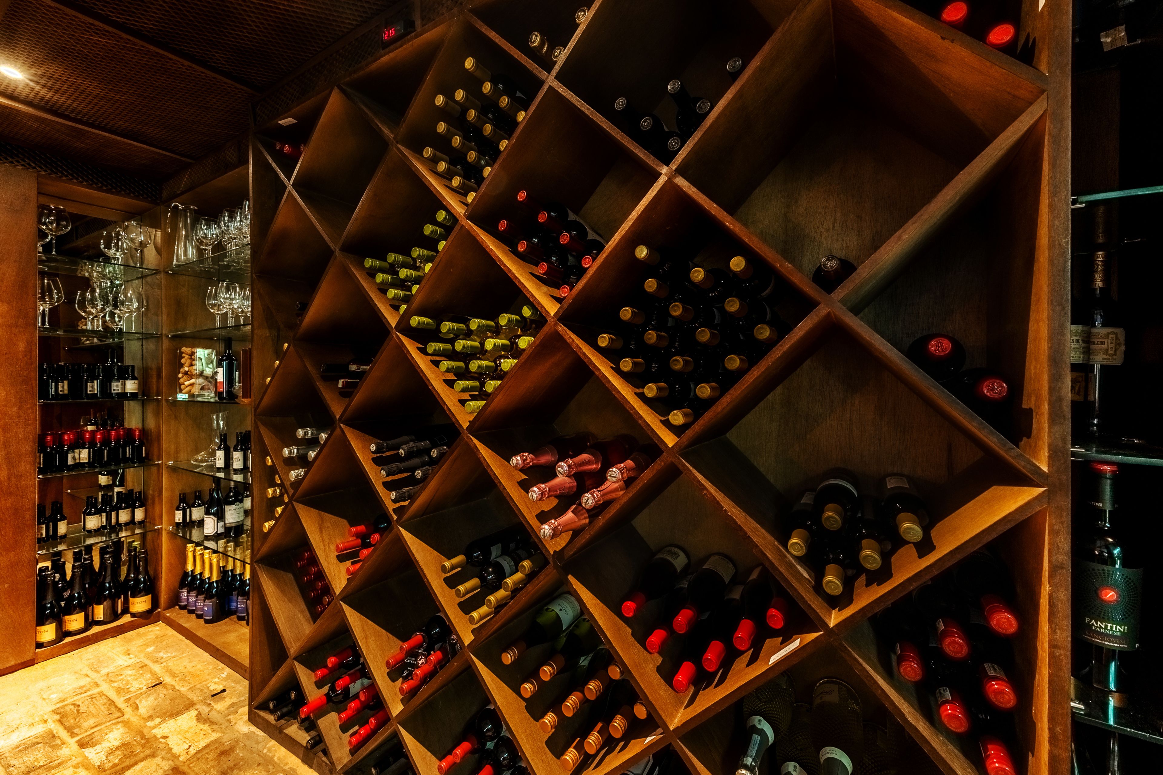 Una bodega con estanterías de madera llenas de botellas de vino y copas.
