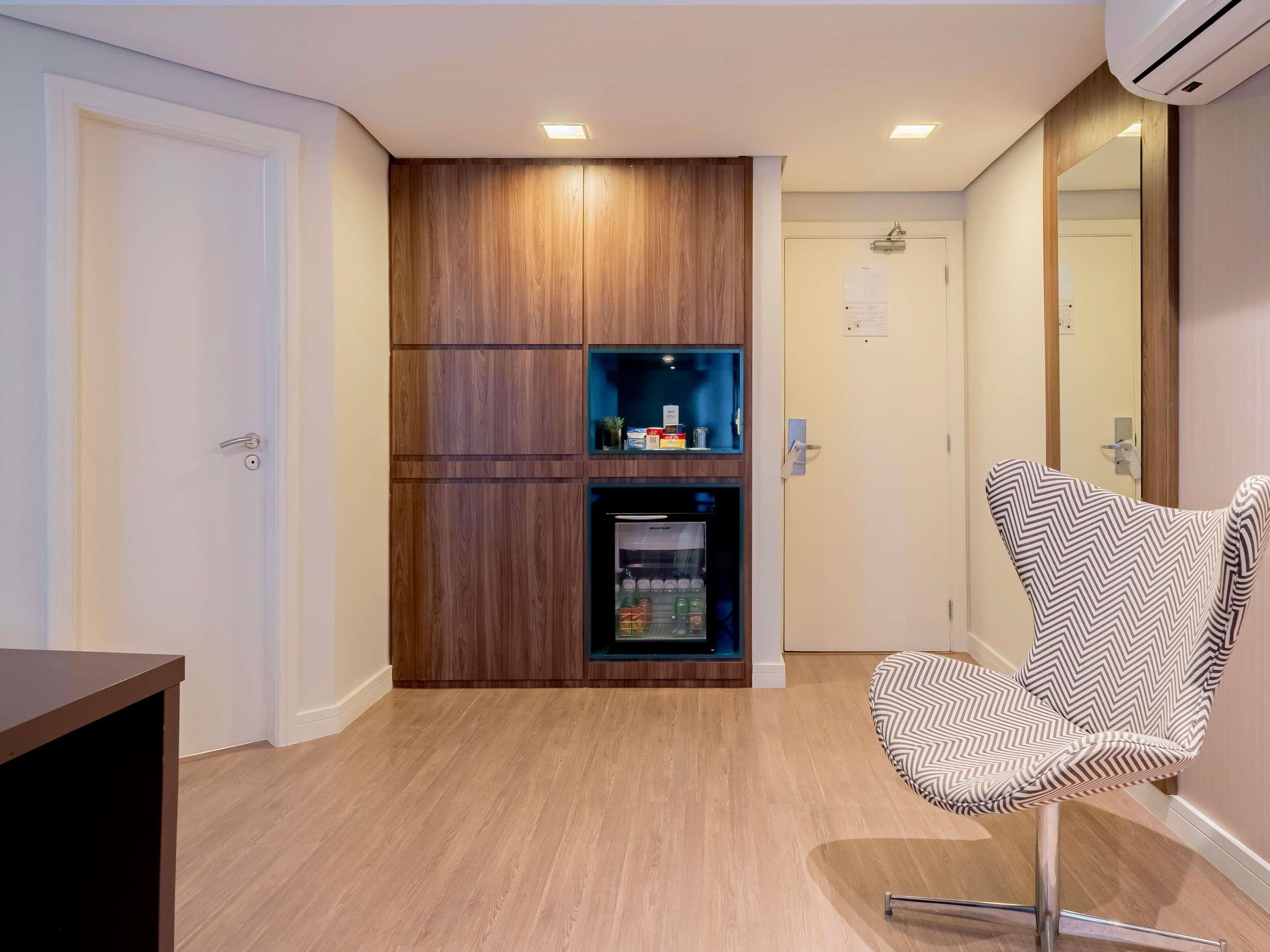 A hotel room with a wooden cabinet, a minibar, and a modern chair.