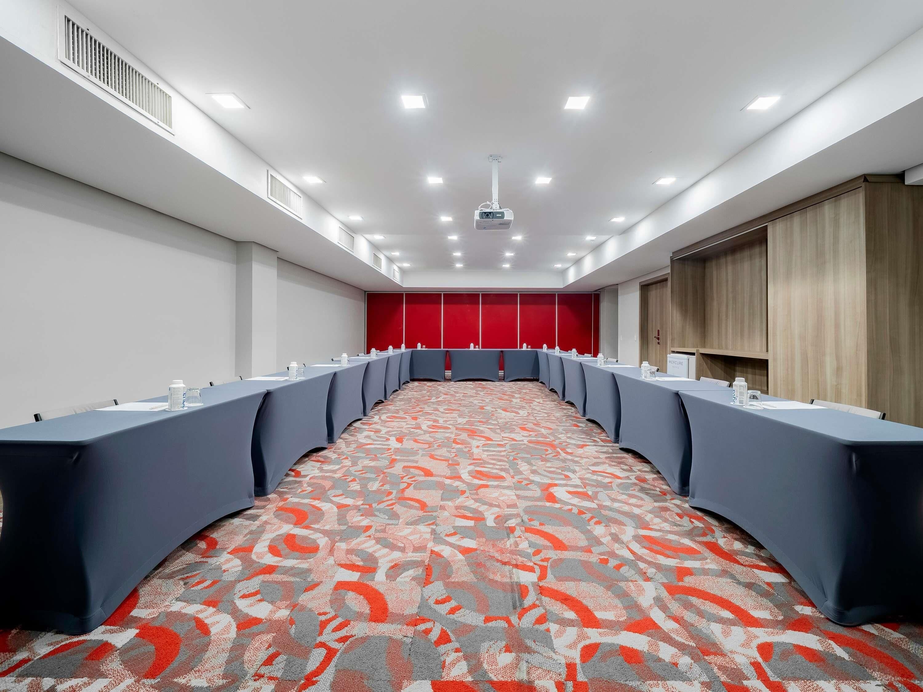 A conference room with a long table, chairs, a projector, and a patterned carpet.