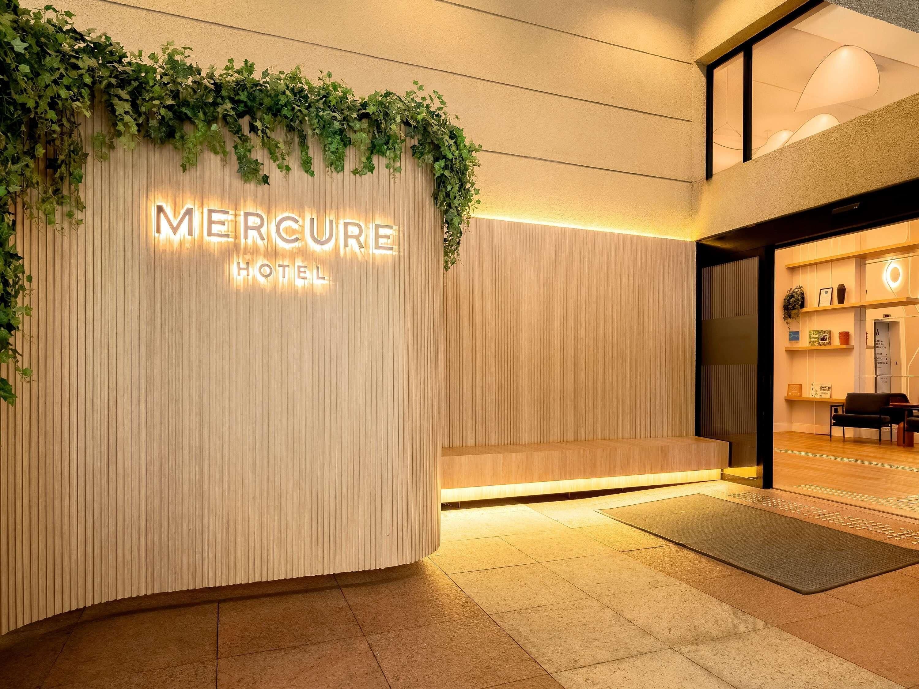 Entrada de un hotel con fachada de madera, un cartel que dice 'Mercure Hotel' y un mostrador de recepción.