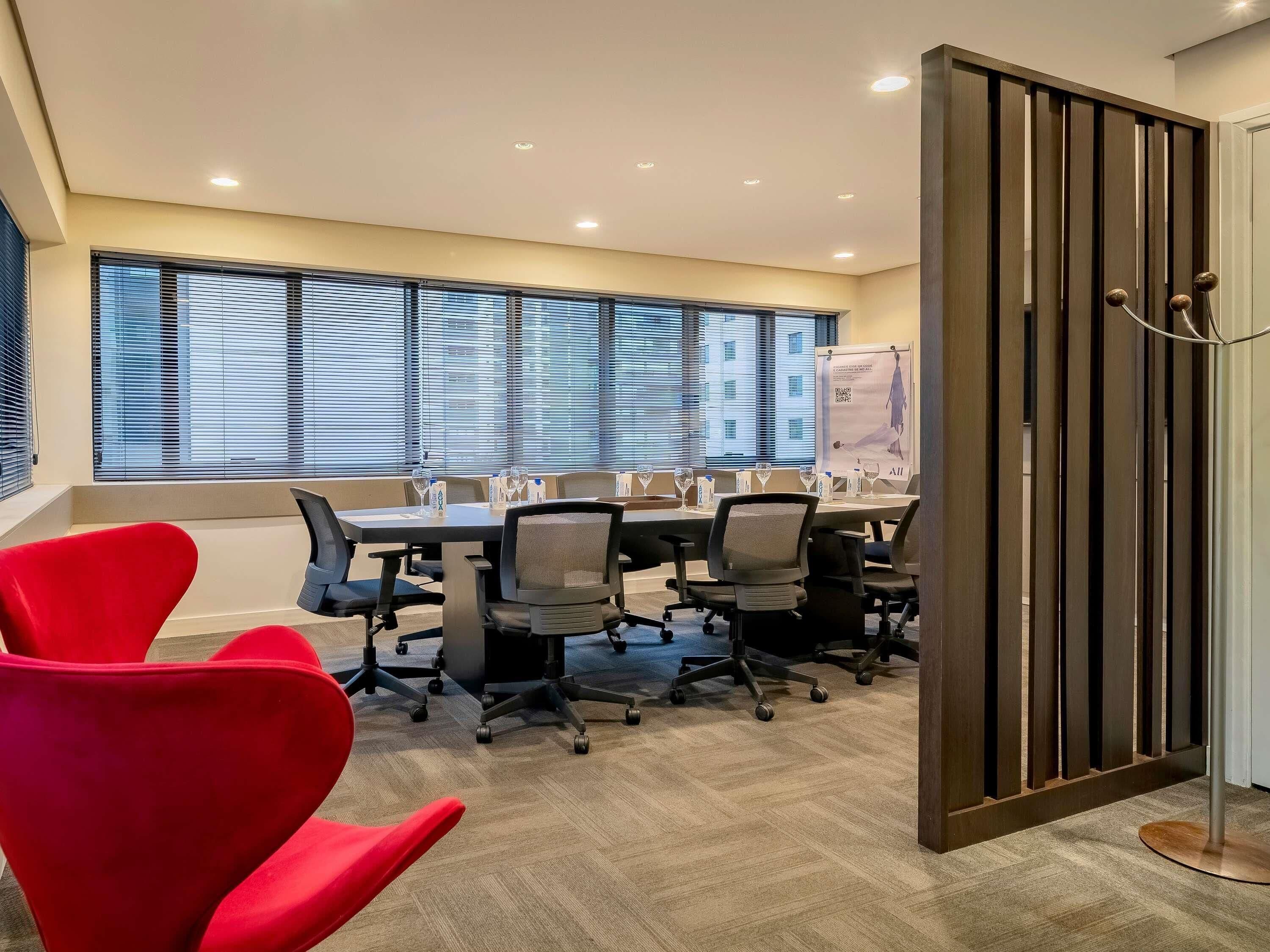 A conference room with a long table, multiple chairs, and a red accent chair.