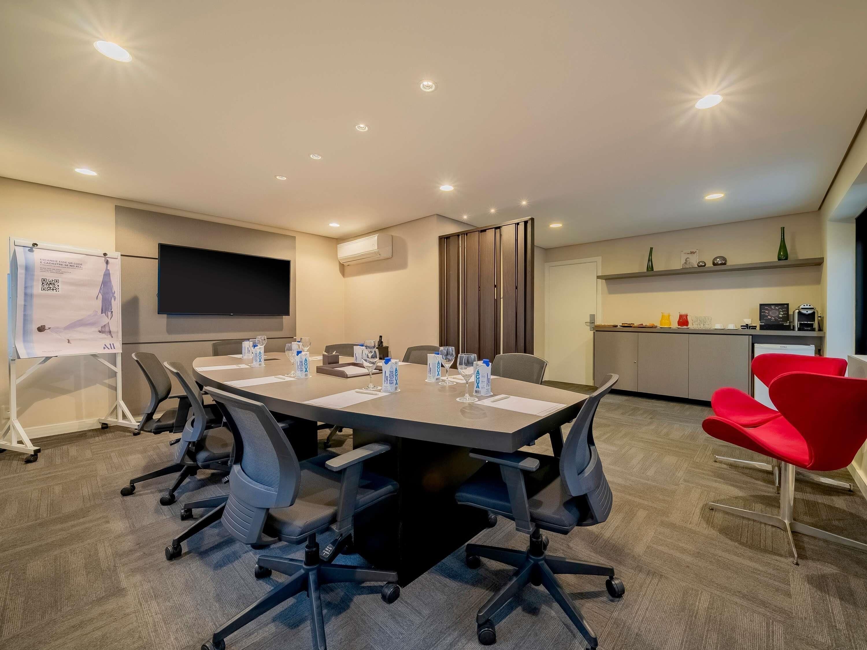A conference room with a large table, chairs, a screen, and a kitchenette.