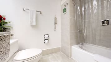 A bathroom with a toilet, a shower with a transparent curtain, and a marble countertop with a plant.