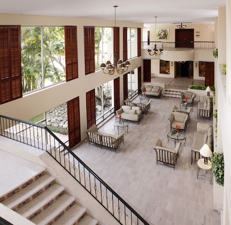 A spacious indoor area with multiple seating arrangements, a staircase, and large windows with shutters.