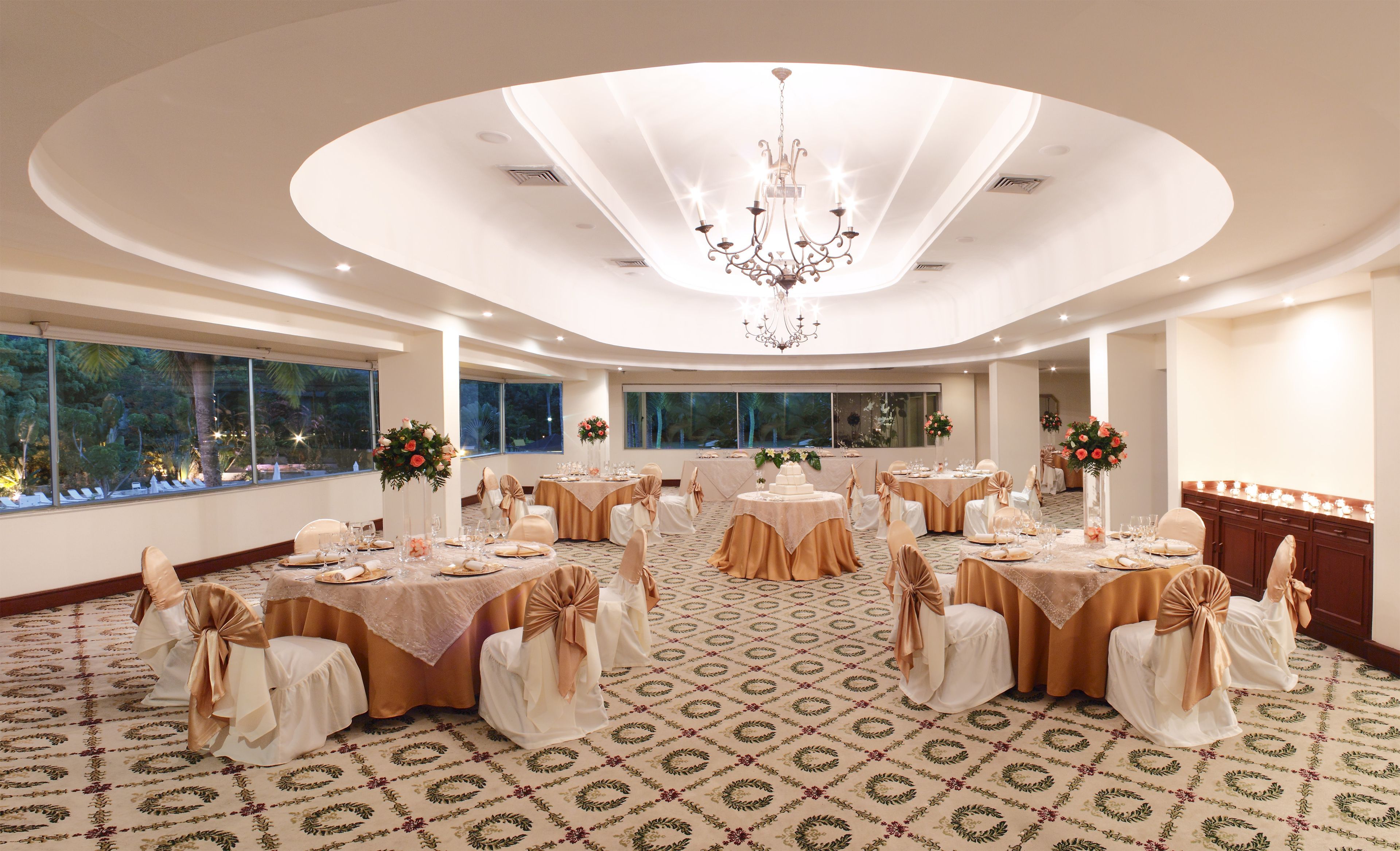 A banquet hall with round tables, chairs, and a chandelier.