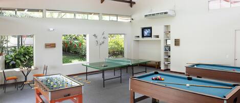 Sala de recreación con mesa de fútbol de mesa, mesa de billar y mesa de sinuca. Ventanas ofrecen luz natural y vistas al exterior.