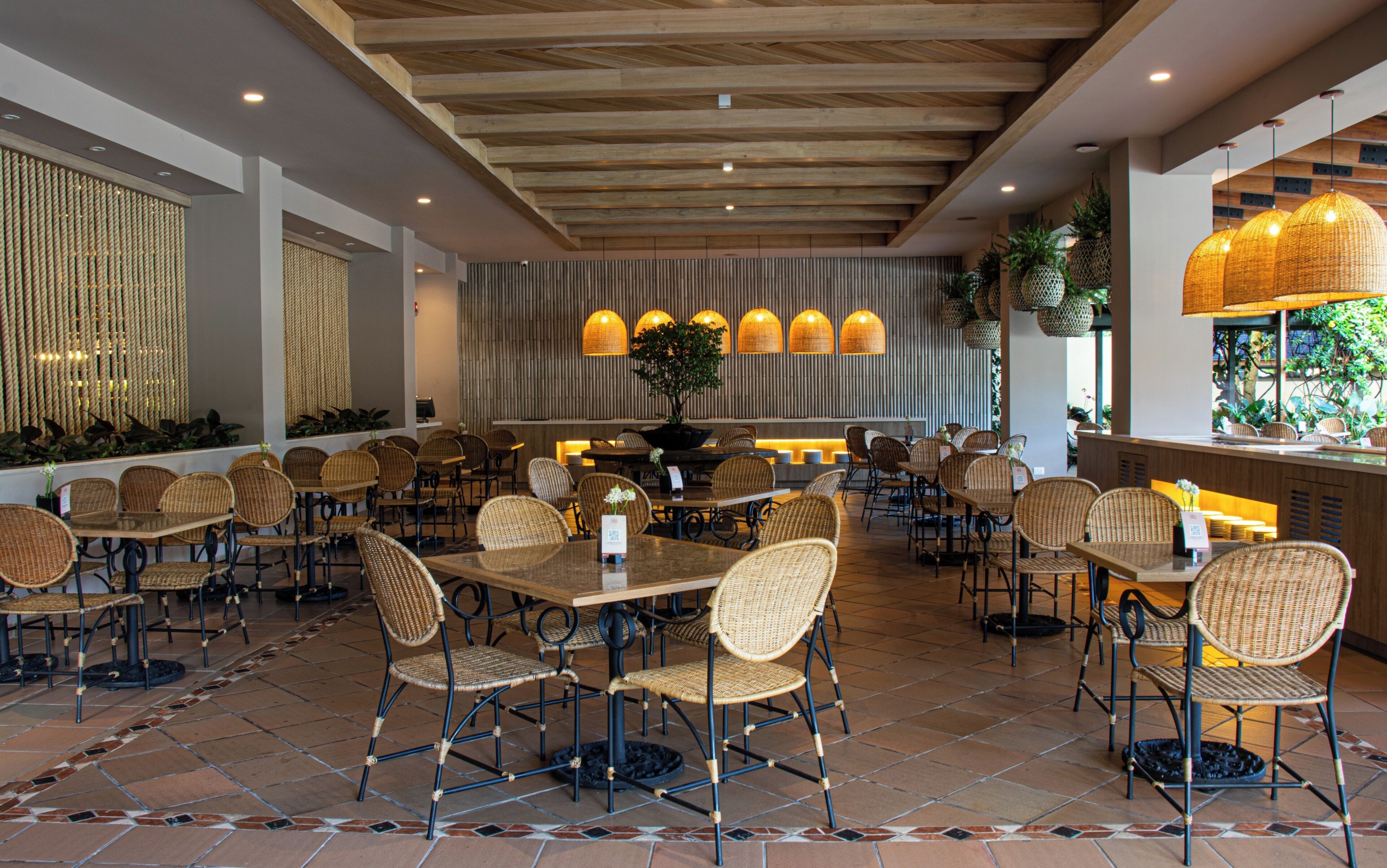 A restaurant with wicker chairs and tables, a tiled floor, and a wooden ceiling.