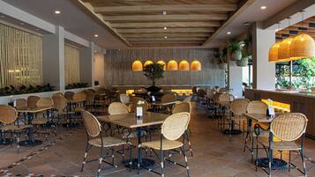 A restaurant with wicker chairs and tables, a tiled floor, and a wooden ceiling.