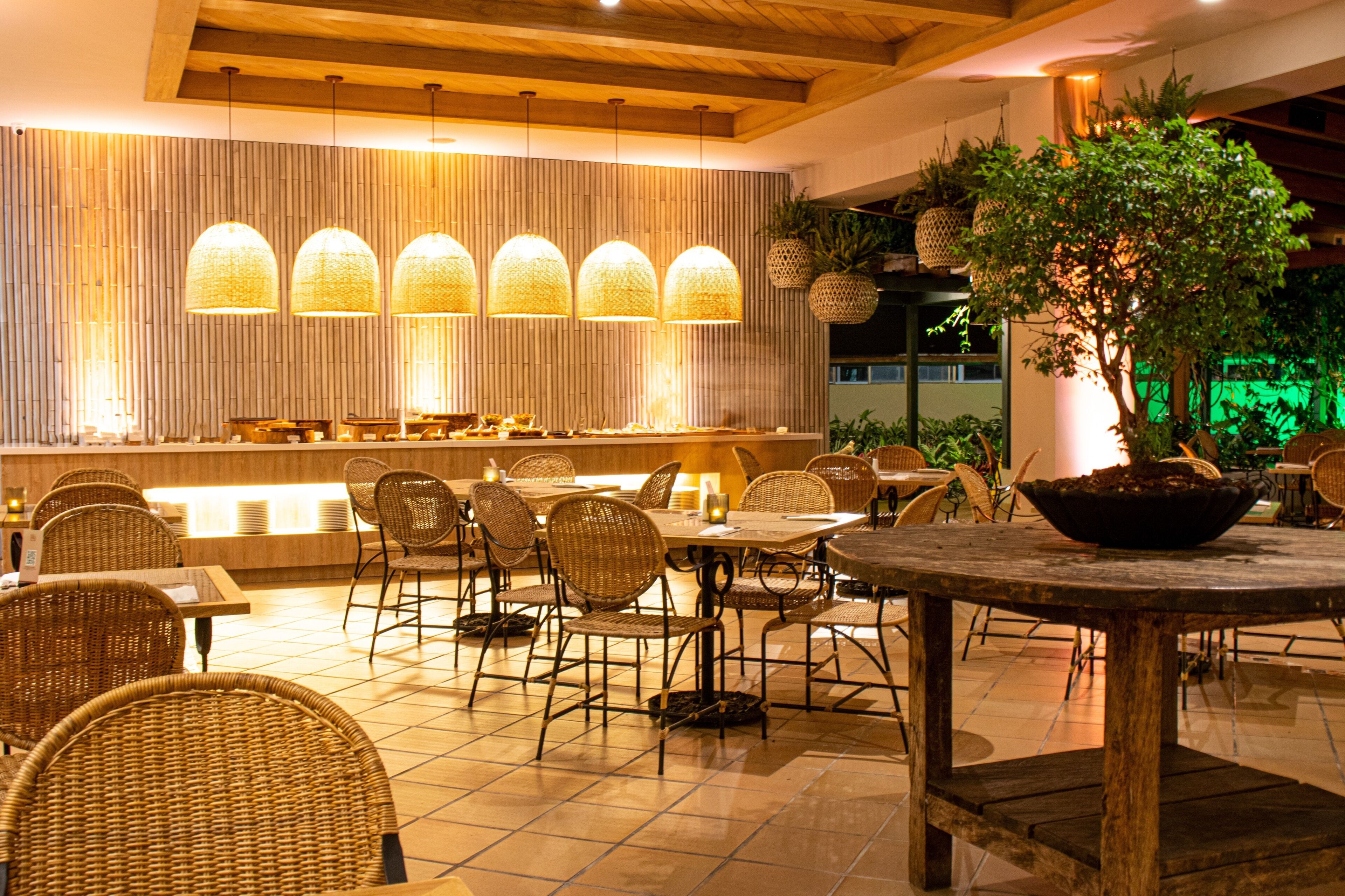 Un restaurante con paredes de bambú, lámparas colgantes, sillas de mimbre y una mesa central con planta en maceta.