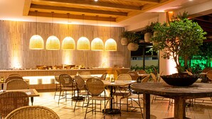 Un restaurante con paredes de bambú, lámparas colgantes, sillas de mimbre y una mesa central con planta en maceta.