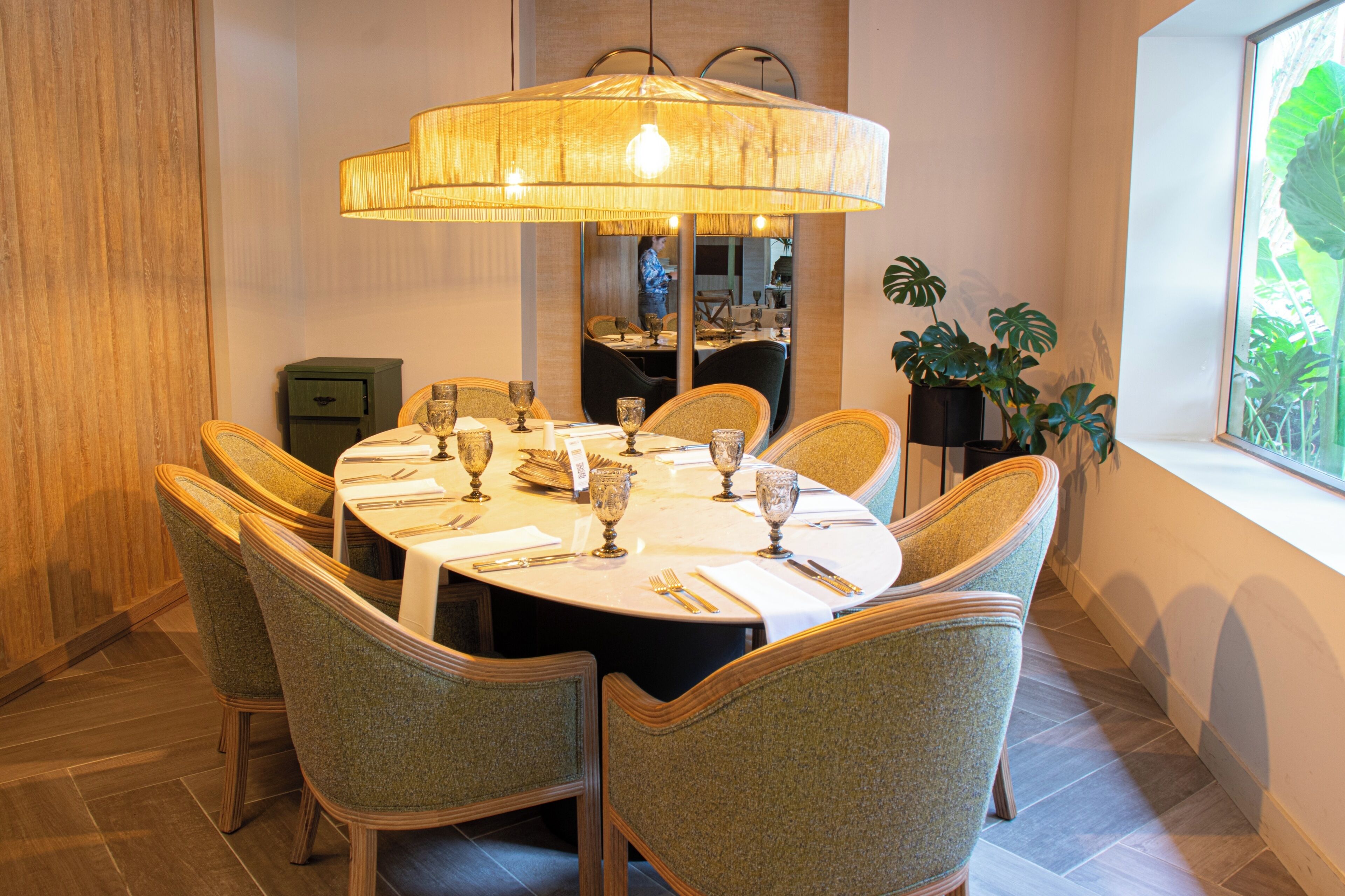 Un coin repas avec une table ronde, des chaises, un luminaire suspendu et une fenêtre agrémentée de plantes.