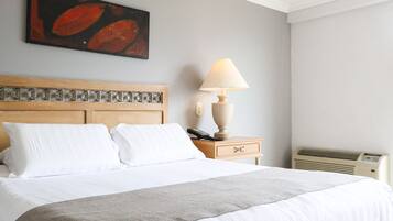 A neatly made bed with white linens and a grey throw blanket, a wooden headboard with a decorative pattern, a bedside lamp, and a wall-mounted painting.