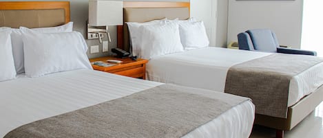 Habitación de hotel con dos camas, una mesita de noche con lámpara, una silla y un cuadro en la pared.