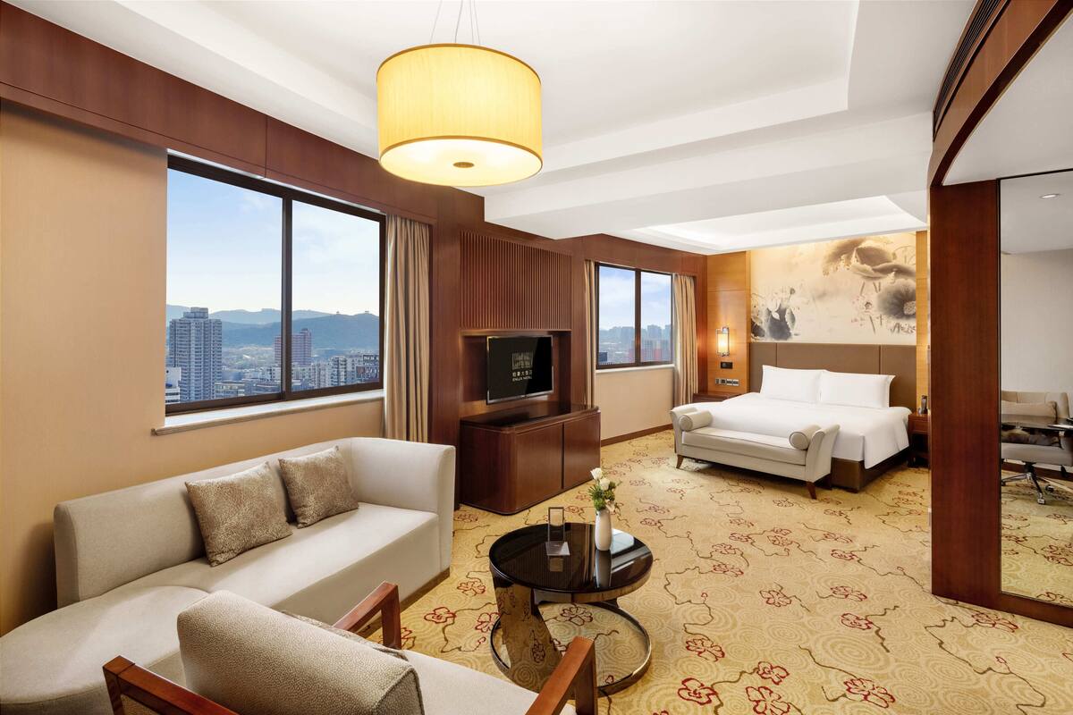 Habitación de hotel con sofá, cama, televisor y ventana grande con vistas a la ciudad.