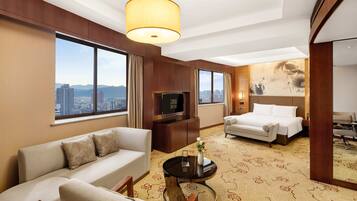 Quarto de hotel com sofá, cama, televisão e uma grande janela com vista para a cidade.