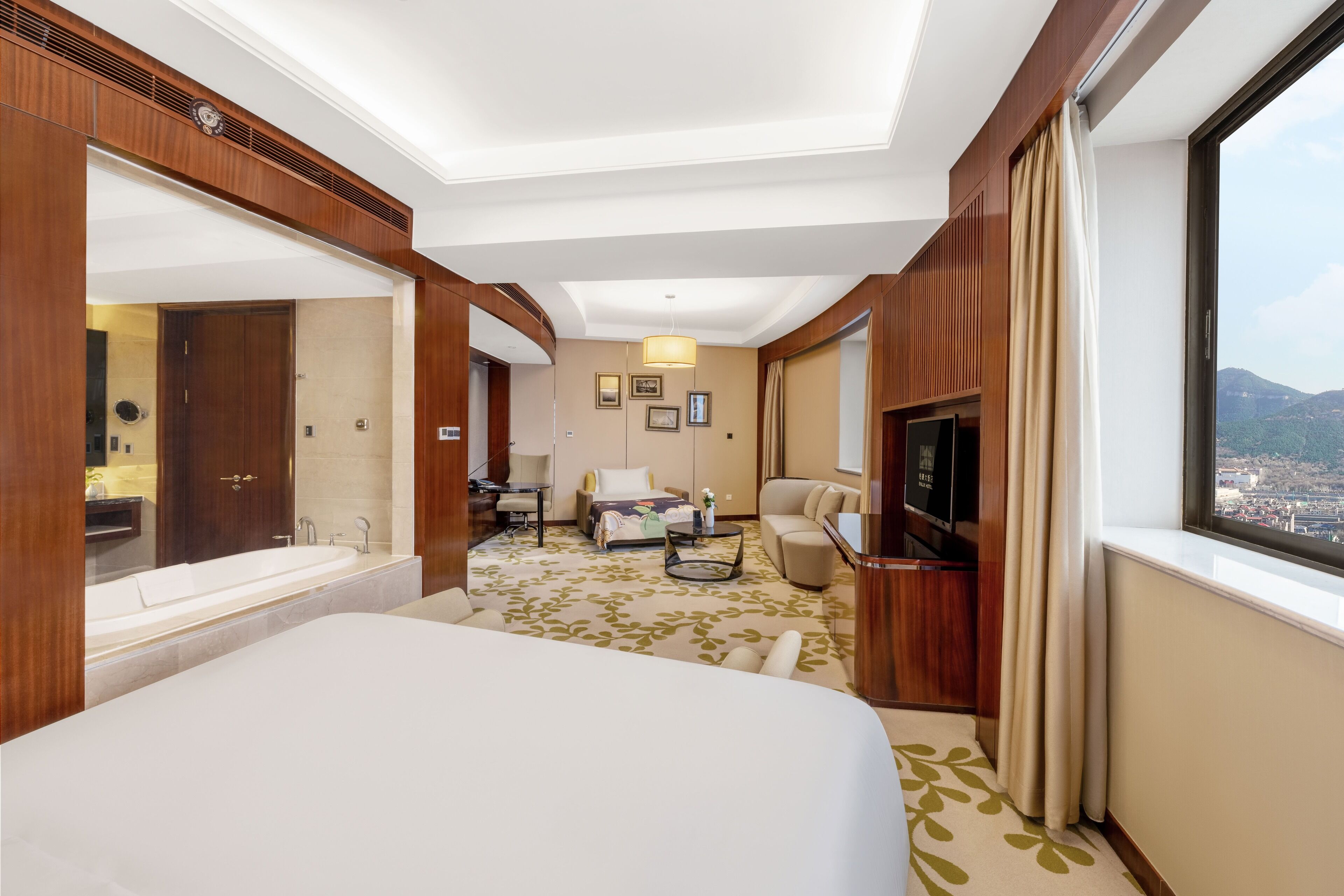 A hotel room with a large bed, a sitting area with a sofa and a coffee table, a television, and a view of the city through a window.