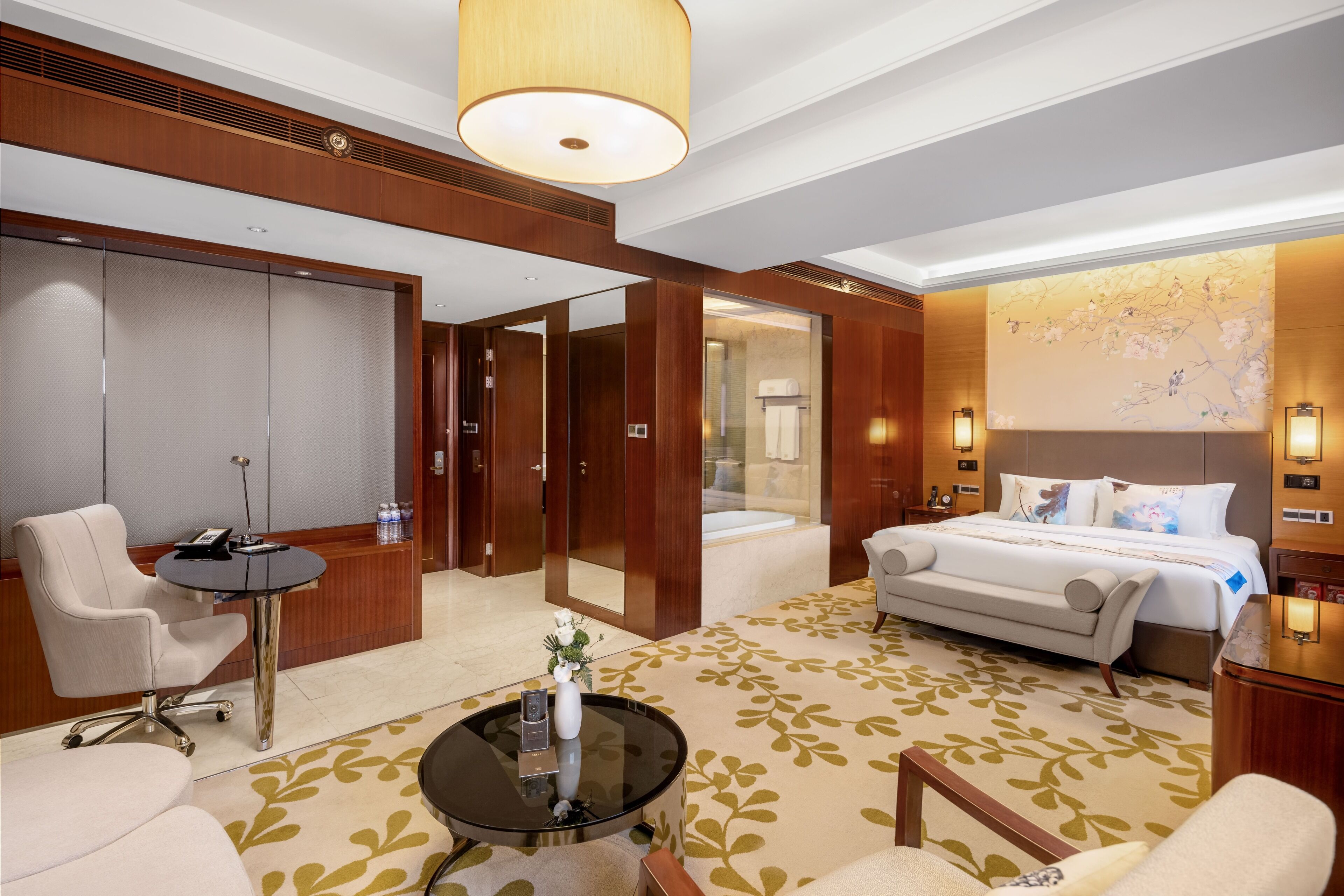 A hotel room with a bed, a sofa, a desk with a chair, a small table, and a mirror.