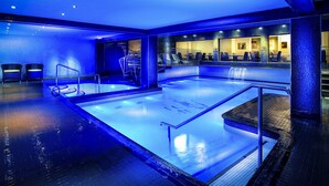A large indoor swimming pool with a blue-lit ceiling and walls, surrounded by seating areas and a staircase. - The Empire Hotel & Spa (Llandudno)