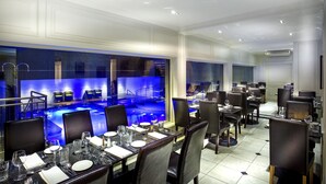 A restaurant with tables set for dining, a pool area with blue lighting, and a modern interior design. - The Empire Hotel & Spa (Llandudno)