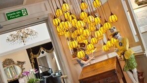 A lobby with a chandelier, a fire exit sign, a mirror, and a statue of a woman. - The Empire Hotel & Spa (Llandudno)