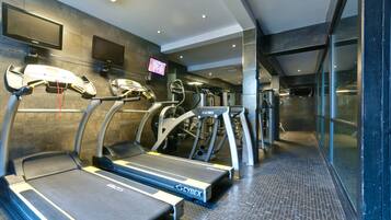 A gym with treadmills, exercise bikes, and a TV screen.