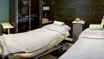 A room with two beds, a small table, a mirror, and a sink.