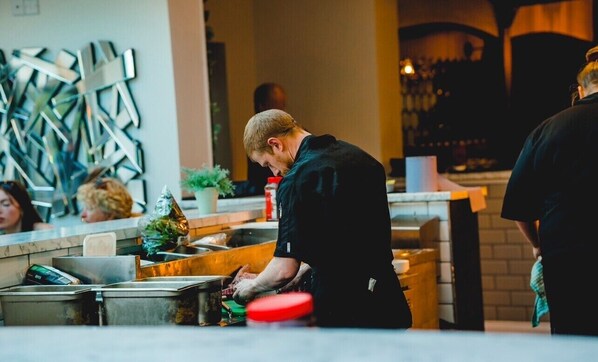 Una persona trabajando en la barra de una cocina moderna con electrodomésticos metálicos y un elemento decorativo en la pared.