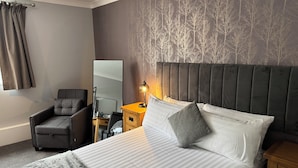 A hotel room with a bed, a chair, a nightstand, a lamp, and a mirror. - The Oaklands Hotel (Norwich)