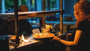 A person serving a pizza at a counter with a window view. - The Oaklands Hotel (Norwich)