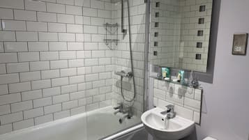 A modern bathroom with white subway tiles, a glass-enclosed shower, a white bathtub, and a sink with a mirror above it.