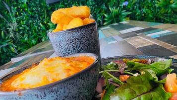 A bowl of soup with a piece of bread on top, a plate of salad, and a sign reading "OAK BAR & TERRACE" in the background.