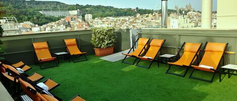 Una terraza en la azotea con césped artificial, sillones de descanso naranja y una planta en maceta.