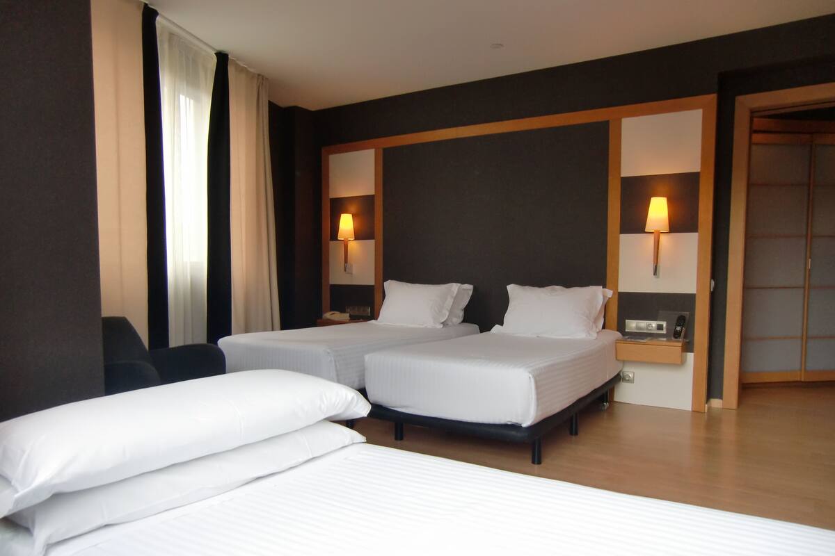 A hotel room with two single beds, a desk with a lamp, and a wardrobe.