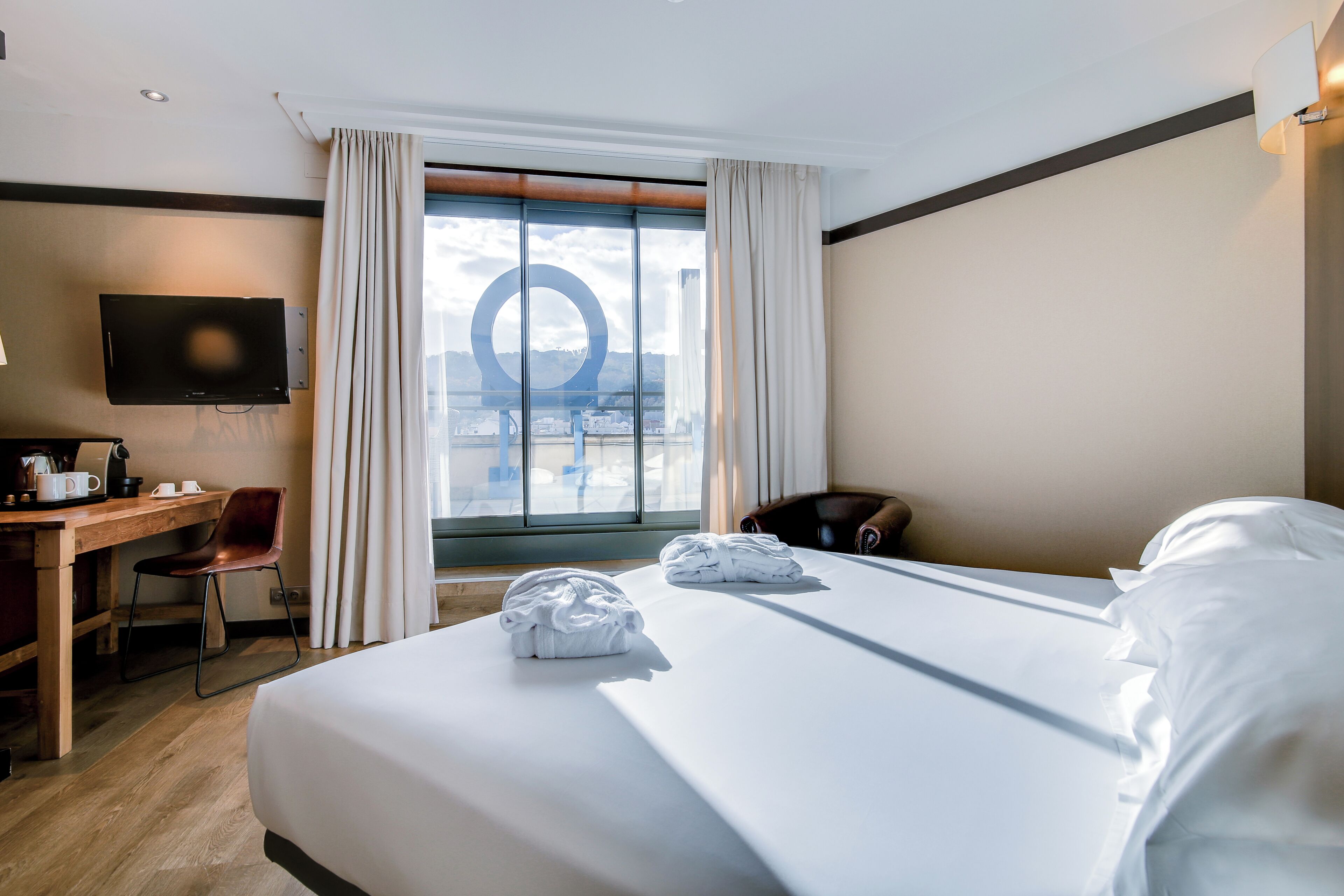 Habitación de hotel con una cama grande, un escritorio con silla, televisión y vistas al exterior a través de una ventana.