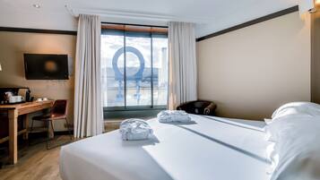 Habitación de hotel con una cama grande, un escritorio con silla, televisión y vistas al exterior a través de una ventana.