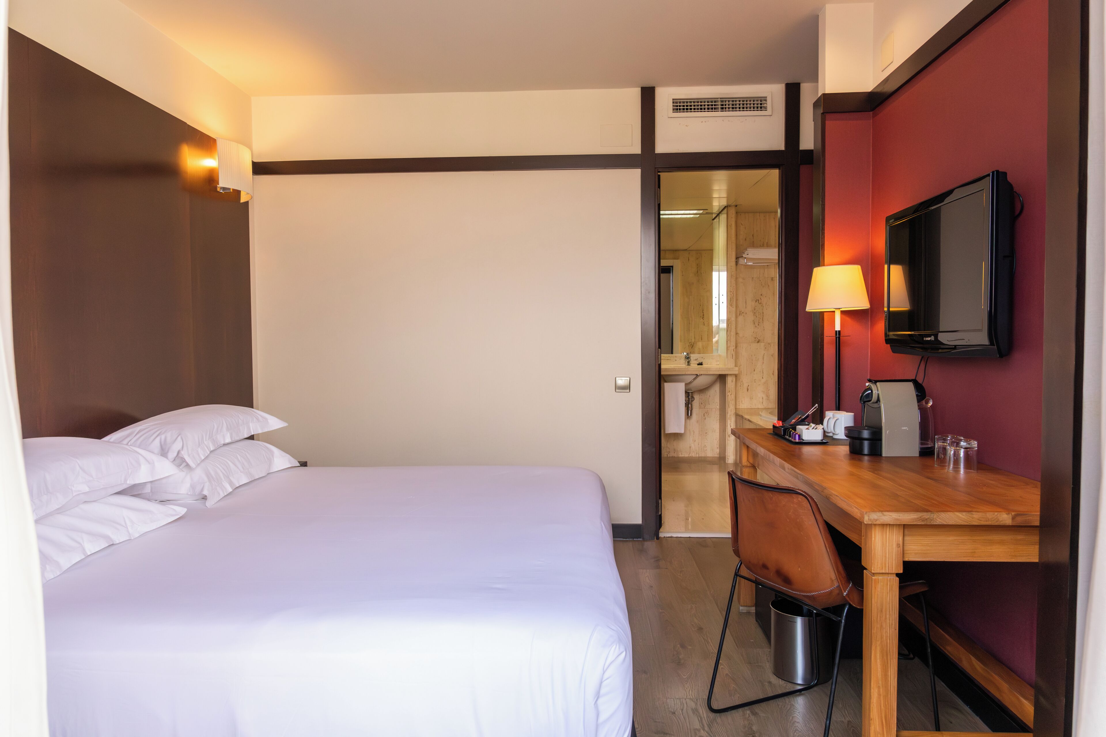 A hotel room with a bed, a desk, a chair, a television, and a lamp.