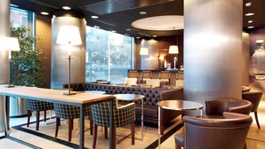 A modern lounge area with a bar, seating, and large windows. - Hotel Barcelona Universal (Barcelona)