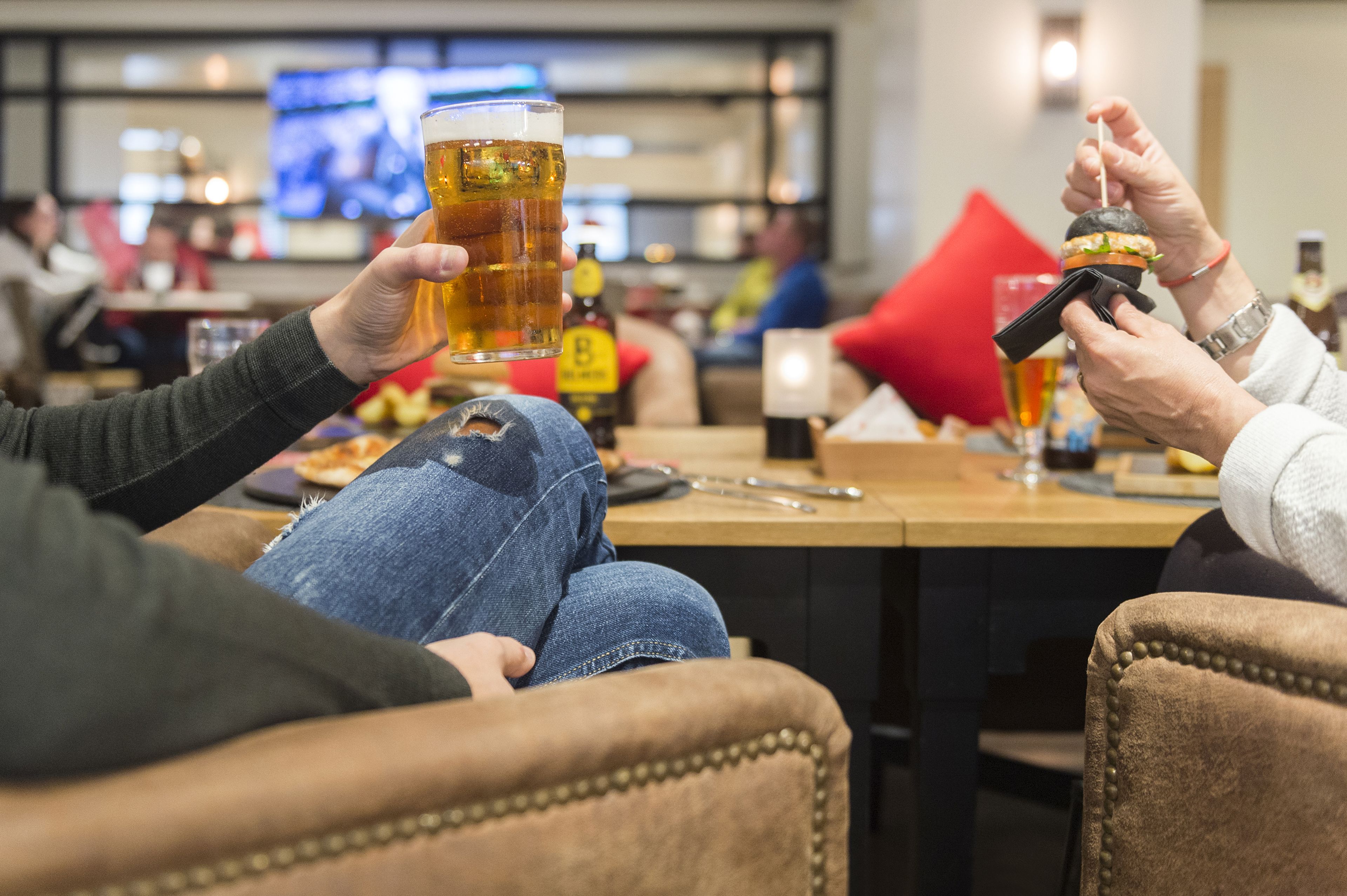 Dos personas sentadas en una mesa de bar, sosteniendo una cerveza y un cóctel.
