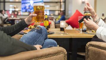Dos personas sentadas en una mesa de bar, sosteniendo una cerveza y un cóctel.